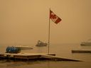 Thick smoke from the Lower East Adams Lake wildfire fills the air and a Canadian flag flies in the wind as RCMP officers on a boat patrol Shuswap Lake, in Scotch Creek, B.C., on Sunday, August 20, 2023.