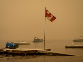 Thick smoke from the Lower East Adams Lake wildfire fills the air and a Canadian flag flies in the wind as RCMP officers on a boat patrol Shuswap Lake, in Scotch Creek, B.C., on Sunday, August 20, 2023.