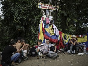 FILE - Migrants sit under a sign marking the Panama-Colombia border during their trek across the Darien Gap, May 9, 2023. Overwhelmed by the resurgence of migrants crossing the Darien jungle on the border with Colombia, the government of Panama announced on Thursday, Aug. 24, 2023, that it will take concrete measures.