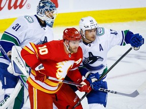 Vancouver Canucks' Noah Juulsen, right, checks Calgary Flames forward Jonathan Huberdeau, centre, as Canucks goalie Artors Silovs looks on during first period NHL preseason hockey action in Calgary on Sunday