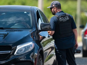 An officer with B.C.'s anti-gang agency, the CFSEU, checks a vehicle approaching a Hell's Angels clubhouse in Langley on July 22, 2023.