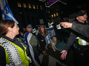 A woman holding an Israeli flag is surrounded by police officers as she shouts at people who were attending a demonstration in support of Palestine, in Vancouver, on Thursday, October 19, 2023.