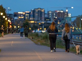 A couple of women walk a dog on the Lachine Canal bike path at dusk, around dinnertime, in Montreal on Friday, Oct. 20, 2023. The days are getting shorter, marking the beginning of a time when many struggle with their mental health.