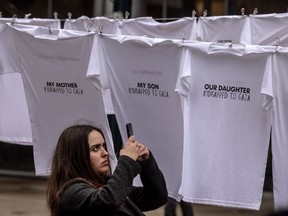 A woman takes a photograph of shirts at Toronto’s David Pecaut Square at an installation called “Threads of Hope” with the names of those taken hostage by Hamas terrorists from Israel to Gaza, Wednesday November 22, 2023.