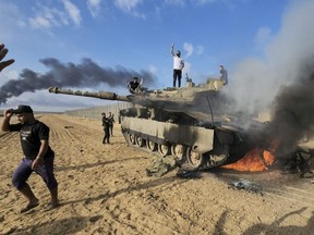 Palestinians celebrate by a destroyed Israeli tank at the Gaza Strip fence east of Khan Younis in southern Israel, Oct. 7, 2023.