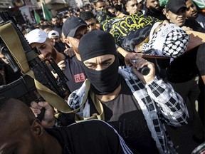 A masked fighter holds up a weapon as mourners carry bodies wrapped with the flag of Palestinian militant group Islamic Jihad, during the funeral of men killed in an overnight Israeli army raid in the Jenin refugee camp, in the occupied West Bank, on November 17, 2023. Israel's army said it killed at least seven militants in two separate confrontations in the West Bank, as Hamas admitted a number of its fighters were slain amid growing violence wracking the occupied territory. (Photo by FADEL SENNA / AFP) (Photo by FADEL SENNA/AFP via Getty Images)
