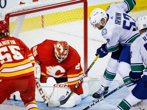 Vancouver Canucks' Matt Irwin, right, digs for the puck as Calgary Flames goalie Jacob Markstrom covers it up during second period NHL preseason hockey action in Calgary Sept. 24, 2023.