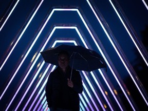 Environment Canada says a "vigorous frontal system" expected to cross British Columbia's south coast is bringing with it heavy rain and wind for some regions of the province, and snow for others, until at least Saturday. A man carrying an umbrella walks through a light tunnel installation during the Lumiere Festival as rain falls in Vancouver,, Monday, Nov. 6, 2023.