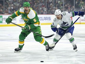 Minnesota Wild defenseman Jake Middleton (5) and Vancouver Canucks right wing Conor Garland (8) compete for the puck during the first period of an NHL hockey game Saturday, Dec. 16, 2023, in St Paul, Minn.
