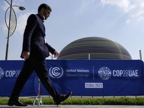 A person walks by a sign for the COP28 UN Climate Summit, Wednesday, Nov. 29, 2023, in Dubai, United Arab Emirates. The world's major climate negotiations risk turning into a trade show spectacle of unchecked corporate influence, some observers warn, as a record number of delegates representing fossil fuel interests descend on the United Nations climate change conference.
