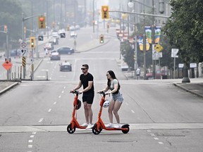People cross Elgin Street on e-scooters in Ottawa, on Sunday, June 25, 2023. The British Columbia government has launched another study to decide how e-scooters fit into the provincial transportation network.