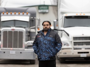 Jatinder Gill stands in front of several semi trucks in his transport yard.