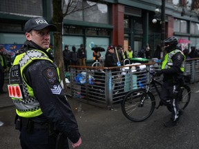 Police officers stand by while an unhoused person collects their belongings as city workers with the assistance of Vancouver police continue for the second day to remove tents and structures from encampments, in the Downtown Eastside of Vancouver, B.C., Thursday, April 6, 2023. British Columbia's Human Rights Commissioner is launching an inquiry into police restrictions on media covering the decampment in Vancouver's Downtown Eastside.