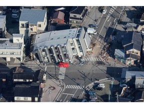 This aerial photo provided by Jiji Press shows a rescue vehicle (C) parked next to a seven-storey building which fell over in Wajima, Ishikawa prefecture on January 2, 2024, a day after a major 7.5 magnitude earthquake struck the Noto region in Ishikawa prefecture.