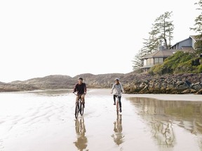 Couple riding bikes along the North Chesterman Beach in Tofino with the Wickaninnish Inn in the background.