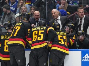 Canucks head coach Rick Tocchet, back centre, and assistant coach Adam Foote, back right, listen as assistant coach Mike Yeo talks to Conor Garland (8), Tyler Myers (57), Ilya Mikheyev (65) and Teddy Blueger (53).