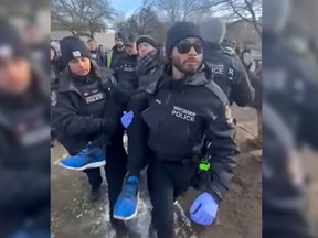 Ryan Sudds, a local advocate and organizer with Stop the Sweeps (blue shoes), is pictured being taken away under arrest by four Vancouver Police officers on Monday, January 15, 2024 in Oppenheimer Park in Vancouver.