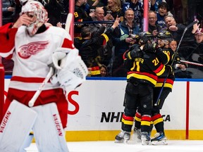 Nils Hoglander and Elias Pettersson celebrate Elias Lindholm's goal as Detroit Red Wings goaltender Alex Lyon looks on during the first period of an NHL game, in Vancouver on Thursday, Feb. 15, 2024.