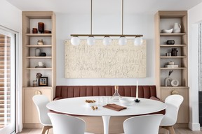 In the dining room, a banquette bench tucks between two built-in cabinets against the wall, maintaining egress to a patio door. Artwork created by the couple's children in earlier years sits opposite a Hayes Linear Chandelier from West Elm.