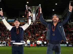 Rob McElhenney, left, and Ryan Reynolds, Owners of Wrexham celebrate with the Vanarama National League trophy as Wrexham win the Vanarama National League and are promoted to the English Football League after victory in the Vanarama National League match between Wrexham and Boreham Wood at Racecourse Ground on April 22, 2023 in Wrexham, Wales.