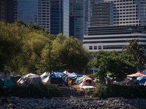 Tents and people are seen at a homeless encampment at Crab Park below the towers of the downtown skyline in Vancouver on Sunday, August 14, 2022. Residents forced out of a Vancouver homeless encampment will be allowed back in this week after the city completed a cleanup of the site.