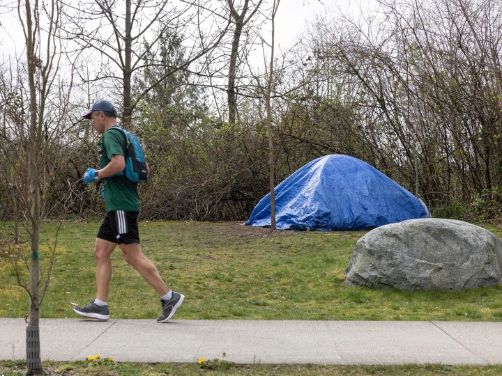  A jogger runs past a homeless person’s shelter erected next to North Grandview Highway in Vancouver, April 6, 2024.