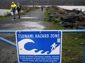 A couple walk along Whiffin Spit Park near a tsunami hazard zone warning sign in Sooke, B.C., on Tuesday, January 23, 2018.