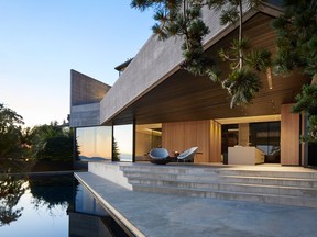 Rather than a flat expanse of glass facing the ocean, the home's levels are staggered, with the upper floor cantilevered over the lower, creating a covered patio below. Sliding glass doors roll wide open to the patio, which leads to an infinity pool overlooking the ocean. An outdoor kitchen and barbecue tuck away behind a subtle wall of flat-panel all-weather cabinets.