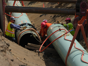 Workers lay pipe during construction of the now-completed Trans Mountain pipeline expansion on farmland in Abbotsford, B.C., on Wednesday, May 3, 2023.