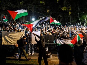 Anti-Israel demonstrators wave flags and hold up smartphones outside the fenced in area of an encampment on the University of Toronto campus on May 2, 2024.