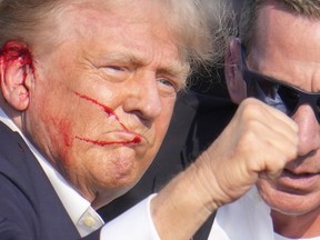 Republican presidential candidate former President Donald Trump gestures as he is surrounded by U.S. Secret Service agents as he is helped off the stage at a campaign rally in Butler, Pa., Saturday, July 13, 2024.