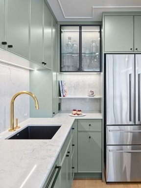 In the kitchen, cabinets painted Farrow & Ball Card Room Green with slim trim add a pop of colour against back-lit glass cabinets, and a Caesarstone quartz backsplash with recessed circular Bocci outlets. A matching quartz-topped island gives the illusion of a heavy slab, but is made out of five pieces with mitred corners.
