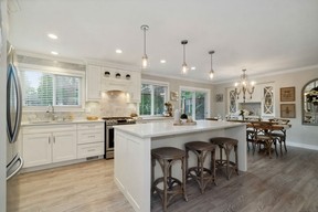 Spacious kitchen boasts white Shaker-style cabinets, stainless-steel appliances, and an island with breakfast bar seating and pendant lighting.