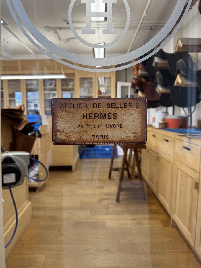  A leather sign on the glass door into a saddlemaking atelier of the French luxury brand Hermès.