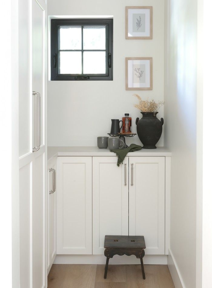  A pantry nook off the kitchen features fresh white cabinetry juxtaposed with an antique stool and vintage treasures.