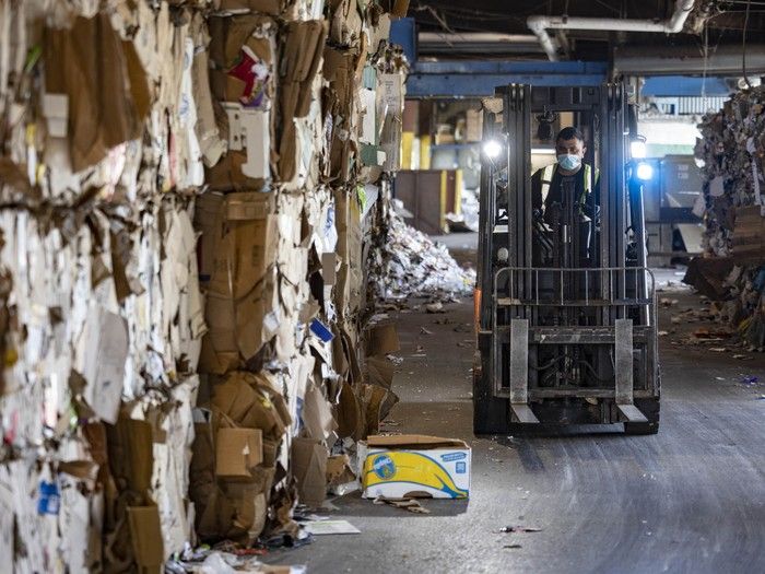 A man on a forklift moves bales of recycled paper.