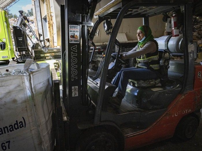 A woman drives a forklift at a recycling depot.