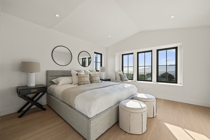  Upstairs, the bright, vaulted primary bedroom is oriented to the views, with a wall of black-framed windows and a soft, neutral palette that keeps the focus on Burrard Inlet and the North Shore.