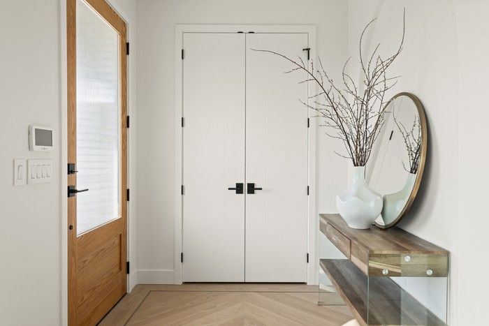  The home’s front entry foyer feels bright, warm, and modern, with chevron wood floors and crisp white walls setting a calm tone. An arch detail in the wall mimics the arched entry outside.