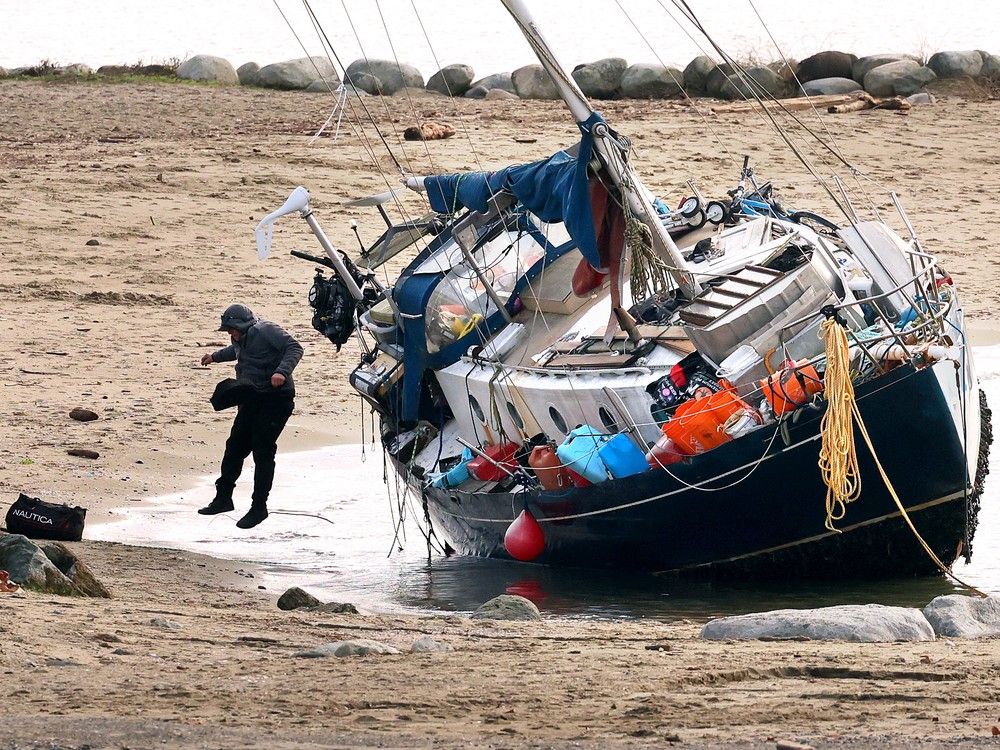 Boat owners remove bags from their beached boat at Sunset Beach following a wind storm in Vancouver on December 17, 2025