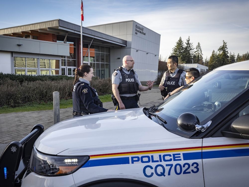 Police stand behind a squad car in front of a school
