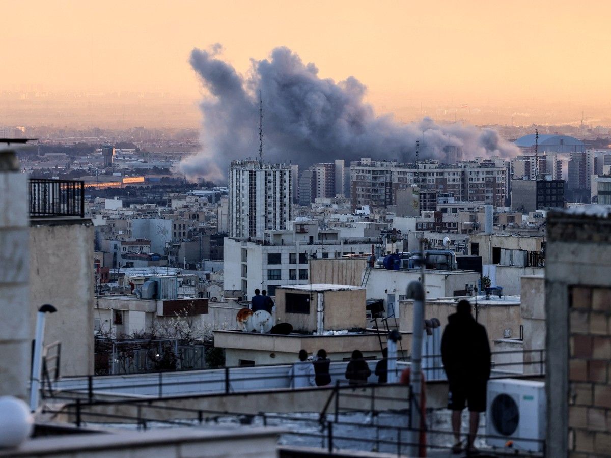  A person stands on the roof of a building looking at a plume of smoke rises after a strike on the Iranian capital Tehran, on March 3, 2026.
