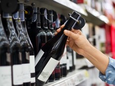 Woman is buying a bottle of wine at the supermarket background.