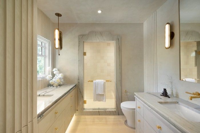In the primary ensuite, custom fluted plaster echoes the living room fireplace, while Fantasy Gold quartzite – fabricated by SSC Countertops – tops the vanities and frames a recessed shower alcove, with matching Apparatus Studio fixtures adding a subtle art deco note. In the primary ensuite, custom fluted plaster echoes the living room fireplace, while Fantasy Gold quartzite – fabricated by SSC Countertops – tops the vanities and frames a recessed shower alcove, with matching Apparatus Studio fixtures adding a subtle art deco note.