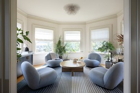 In a sunlit lounge space, low-profile blue armchairs from Inform Interiors centre around a round coffee table, flanked by bay windows and softened by a mix of vintage and custom pieces.