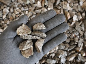 Hand with protective glove holding pieces of pentlandite ore.