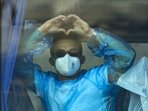 A man with a mask holds his hands in a heart shape