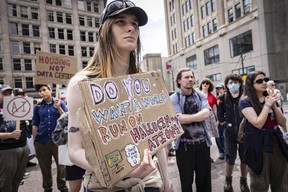 A protester holds a cardboard sign asking 'do you want a world run on hallucinations?'