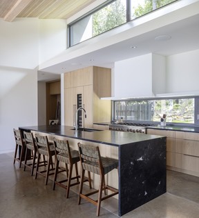 White oak millwork keeps the kitchen warm and quietly understated, while a long island topped with honed Infinity Black quartzite from Bourdignon creates space for meal prep and conversation. Risom counter stools by Knoll line one side, while clerestory windows draw natural light deep into the room. For Westcoast Homes 0620 design profile of Savary Island property designed by Vancouver's Balcaen Kwan Architecture and Design.