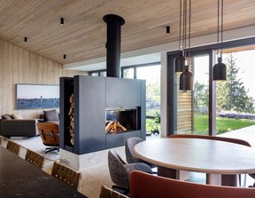 In the main cabin, a two-sided wood-burning fireplace by Stûv divides the living and dining areas without interrupting flow. Mid-century modern-inspired furniture and lighting contrasts the more rustic feel of the woods. Curved Sendai seating by Minotti and a custom dining table by Vancouver furnituremaker Lock & Mortise bring a soft counterpoint to the cabin's clean-lined architecture, under blackened brass Aria pendants by Allied Maker.